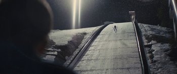 Movie still from “Eddie the Eagle” (2015), directed by Dexter Fletcher – A person is skiing down a snowy slope; Extreme Wide shot, High angle