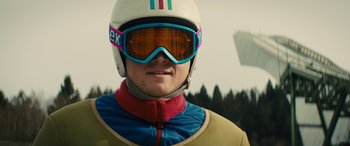 Movie still from “Eddie the Eagle” (2015), directed by Dexter Fletcher – A man wearing goggles and a helmet; Medium shot, Low angle