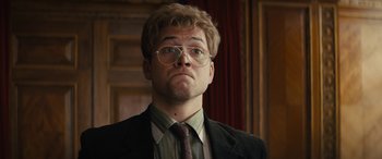 Movie still from “Eddie the Eagle” (2015), directed by Dexter Fletcher – A man in a suit and tie wearing glasses; Close Up shot, Low angle
