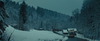 Movie still from “Eddie the Eagle” (2015), directed by Dexter Fletcher – A bus driving down a snow covered road next to a forest; Extreme Wide shot, High angle