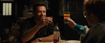 Movie still from “Eddie the Eagle” (2015), directed by Dexter Fletcher – A man sitting at a table holding a glass of wine; Medium shot, Over the shoulder angle