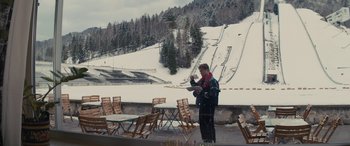 Movie still from “Eddie the Eagle” (2015), directed by Dexter Fletcher – A man standing in front of a ski slope; Wide shot, Over the shoulder angle