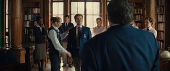 Movie still from “Eddie the Eagle” (2015), directed by Dexter Fletcher – A group of young men standing around each other in front of a window; Medium shot, Over the shoulder angle