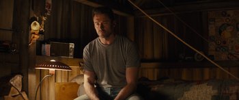 Movie still from “Eddie the Eagle” (2015), directed by Dexter Fletcher – A man sitting on a couch in a room; Medium shot, Low angle