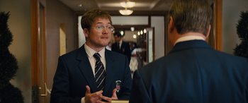 Movie still from “Eddie the Eagle” (2015), directed by Dexter Fletcher – A man in a suit and tie talking to another man; Medium shot, Over the shoulder angle