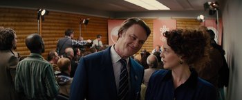 Movie still from “Eddie the Eagle” (2015), directed by Dexter Fletcher – A man and a woman are talking to each other in front of an audience; Medium shot, Over the shoulder angle