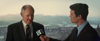 Movie still from “Eddie the Eagle” (2015), directed by Dexter Fletcher – Two men in suits and ties are holding microphones; Medium shot, Over the shoulder angle