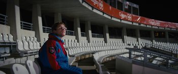 Movie still from “Eddie the Eagle” (2015), directed by Dexter Fletcher – A man sitting in front of an empty bleachers; Wide shot, Low angle