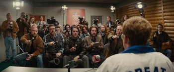 Movie still from “Eddie the Eagle” (2015), directed by Dexter Fletcher – A group of people sitting in front of microphones; Medium shot, Over the shoulder angle