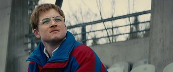 Movie still from “Eddie the Eagle” (2015), directed by Dexter Fletcher – A person wearing glasses and a jacket; Close Up shot, Low angle