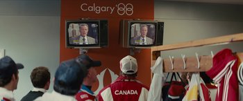 Movie still from “Eddie the Eagle” (2015), directed by Dexter Fletcher – Two men watching television in a room; Medium shot, Over the shoulder angle