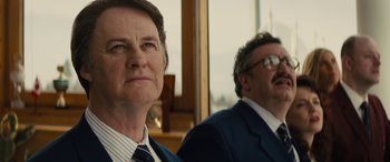 Movie still from “Eddie the Eagle” (2015), directed by Dexter Fletcher – A man and a woman in business suits looking at the camera; Close Up shot, Low angle