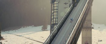 Movie still from “Eddie the Eagle” (2015), directed by Dexter Fletcher – A person is skiing down a ski slope; Extreme Wide shot, Low angle