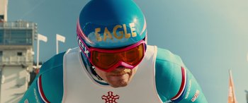 Movie still from “Eddie the Eagle” (2015), directed by Dexter Fletcher – A person wearing a helmet and goggles; Close Up shot, Over the shoulder angle