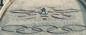 Movie still from “Eddie the Eagle” (2015), directed by Dexter Fletcher – A person in a blue suit is skiing in the water; Extreme Wide shot, Overhead angle