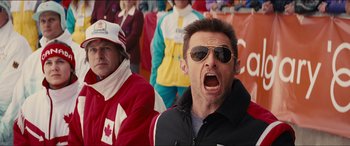 Movie still from “Eddie the Eagle” (2015), directed by Dexter Fletcher – A man in sunglasses and a canadian flag jacket is screaming; Medium shot, Low angle