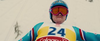 Movie still from “Eddie the Eagle” (2015), directed by Dexter Fletcher – A man wearing a helmet , goggles , and a ski jacket; Medium shot, Low angle
