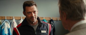 Movie still from “Eddie the Eagle” (2015), directed by Dexter Fletcher – A person wearing a jacket near a wall; Close Up shot, Over the shoulder angle