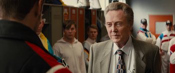 Movie still from “Eddie the Eagle” (2015), directed by Dexter Fletcher – A group of men standing next to each other in a room; Close Up shot, Over the shoulder angle
