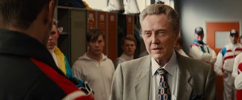 Movie still from “Eddie the Eagle” (2015), directed by Dexter Fletcher – A man in a suit standing next to two other men; Close Up shot, Over the shoulder angle