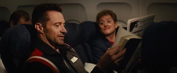 Movie still from “Eddie the Eagle” (2015), directed by Dexter Fletcher – Two men sitting on an airplane looking at a book; Close Up shot, Over the shoulder angle