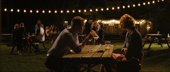 Movie still from “Eden Lake” (2008), directed by James Watkins – A man sitting at a picnic table drinking a beer; Medium shot, Over the shoulder angle