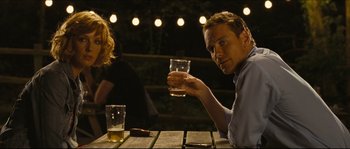 Movie still from “Eden Lake” (2008), directed by James Watkins – A man sitting at a table holding a glass of beer; Medium shot, Low angle
