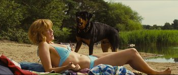 Movie still from “Eden Lake” (2008), directed by James Watkins – A woman in a bikini laying on the beach next to a dog; Medium shot, Low angle