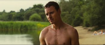 Movie still from “Eden Lake” (2008), directed by James Watkins – A shirtless man standing next to a body of water; Medium shot, Low angle
