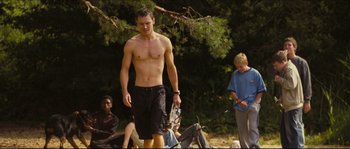 Movie still from “Eden Lake” (2008), directed by James Watkins – A man standing in the grass holding a tennis racket; Medium shot, Low angle