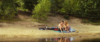 Movie still from “Eden Lake” (2008), directed by James Watkins – A man and a woman sitting on a blanket on the beach; Wide shot, High angle