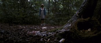 Movie still from “Eden Lake” (2008), directed by James Watkins – A woman standing in the woods near a bottle; Wide shot, Low angle