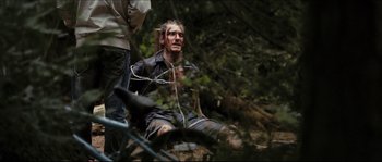 Movie still from “Eden Lake” (2008), directed by James Watkins – A man chained to a tree in the woods; Medium shot, Over the shoulder angle