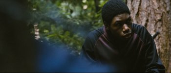 Movie still from “Eden Lake” (2008), directed by James Watkins – A man sitting in the woods with trees in the background; Close Up shot, Over the shoulder angle