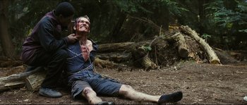 Movie still from “Eden Lake” (2008), directed by James Watkins – A man with a chain around his neck is chained to a tree; Medium shot, Over the shoulder angle
