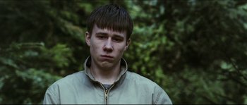 Movie still from “Eden Lake” (2008), directed by James Watkins – A young man in a tan jacket is standing in front of a tree; Close Up shot, Low angle