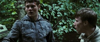 Movie still from “Eden Lake” (2008), directed by James Watkins – A young man with blood on his face stands in front of a tree; Medium shot, Over the shoulder angle
