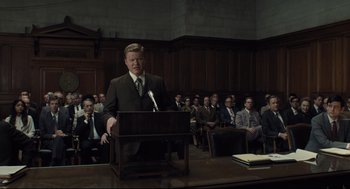 Movie still from “The Post” (2017), directed by Steven Spielberg – A man in a suit is speaking in front of a group of people; Medium shot, Over the shoulder angle