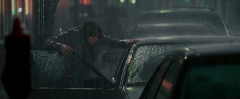 Movie still from “Edge of Darkness” (2010), directed by Martin Campbell – A woman leaning on the hood of a car in the pouring rain; Medium shot, High angle
