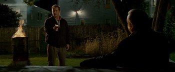 Movie still from “Edge of Darkness” (2010), directed by Martin Campbell – A man standing in the grass holding a cell phone; Medium shot, Over the shoulder angle