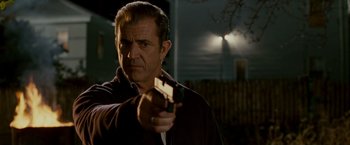 Movie still from “Edge of Darkness” (2010), directed by Martin Campbell – A man holding a gun while standing in a yard at night; Close Up shot, Over the shoulder angle