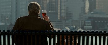 Movie still from “Edge of Darkness” (2010), directed by Martin Campbell – A man sitting on a bench holding a glass of wine; Medium shot, Over the shoulder angle