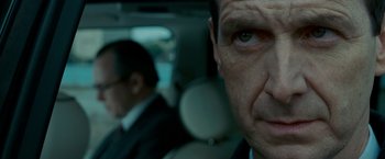 Movie still from “Edge of Darkness” (2010), directed by Martin Campbell – A man in a suit and tie sitting in a car looking at the camera; Close Up shot, Over the shoulder angle