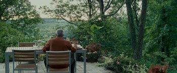 Movie still from “Edge of Darkness” (2010), directed by Martin Campbell – An older man sitting at a table in a garden; Wide shot, High angle