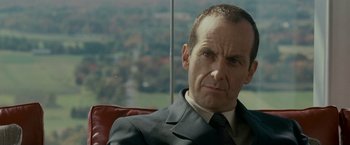 Movie still from “Edge of Darkness” (2010), directed by Martin Campbell – A man in a suit sitting in a red chair; Close Up shot, Over the shoulder angle