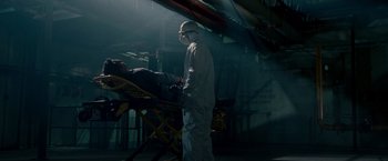 Movie still from “Edge of Darkness” (2010), directed by Martin Campbell – A man wearing a mask is standing next to an ambulance; Wide shot, Low angle