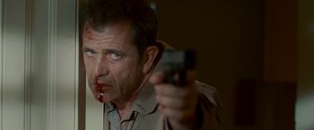 Movie still from “Edge of Darkness” (2010), directed by Martin Campbell – A person holding a gun with blood on his face; Close Up shot, Over the shoulder angle