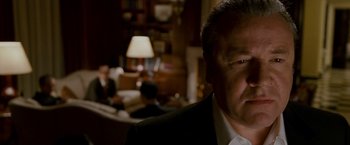 Movie still from “Edge of Darkness” (2010), directed by Martin Campbell – A man in a suit and tie in front of a living room; Close Up shot, Over the shoulder angle