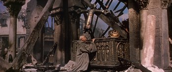 Movie still from “El Cid” (1961), directed by Anthony Mann – An old man in a monk's outfit is standing next to an ornate structure; Wide shot, Low angle