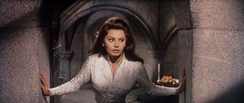 Movie still from “El Cid” (1961), directed by Anthony Mann – A beautiful woman in a white dress standing in front of a stone wall; Medium shot, Low angle